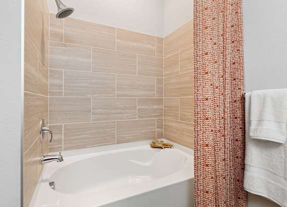 A white bathtub with a shower head and a towel hanging on the wall.