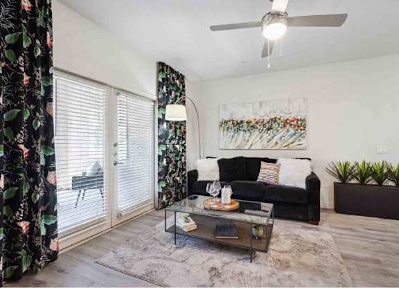 A living room with a black couch, a glass coffee table, and a painting on the wall.