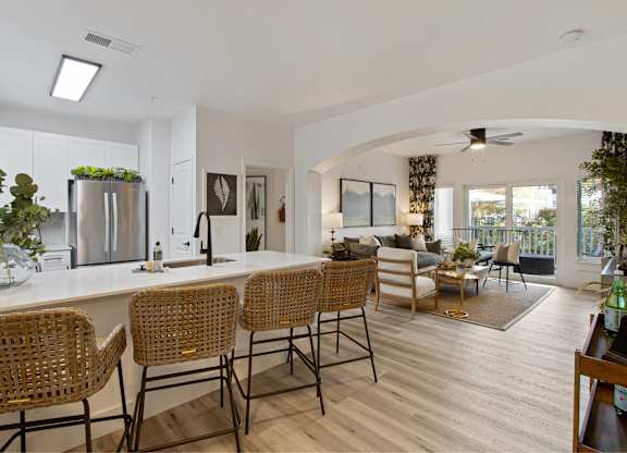 the kitchen and living room of a house with a large white counter and bar chairs
