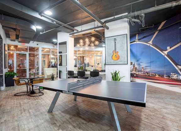 A ping pong table is in the middle of a room with a guitar hanging on the wall.