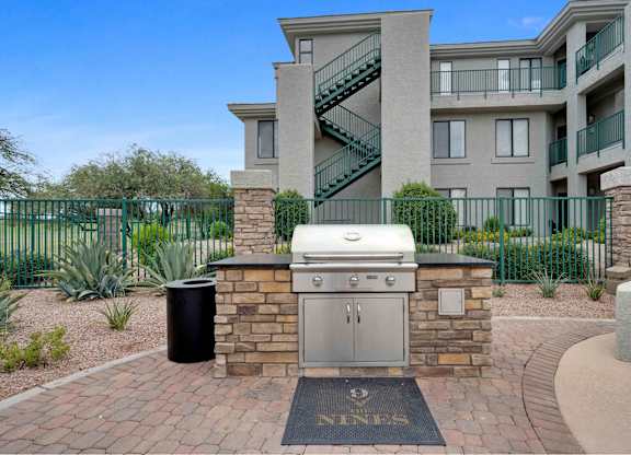 an outdoor kitchen with a grill and a trash can in front of an apartment building