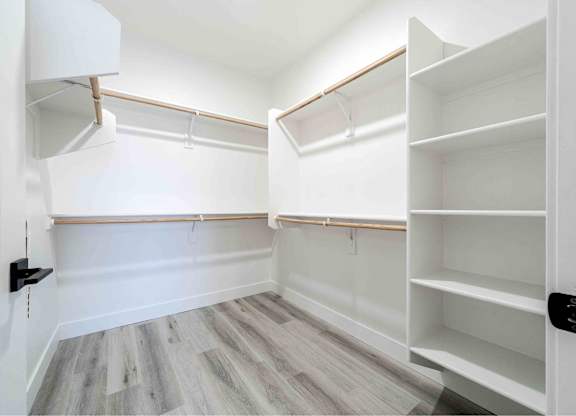 a walk in closet with white walls and wooden floors