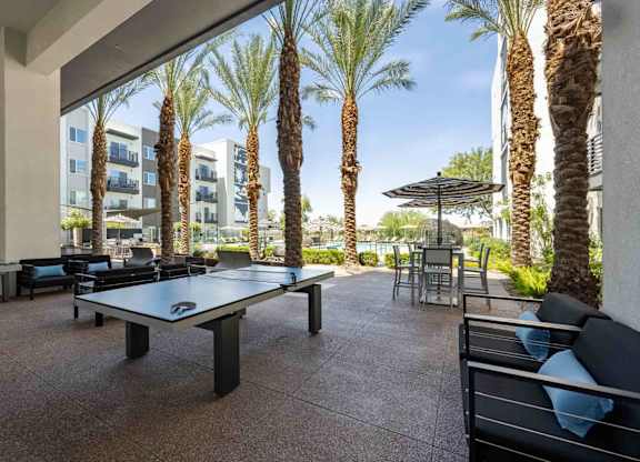 a patio with a ping pong table and chairs with palm trees in the background