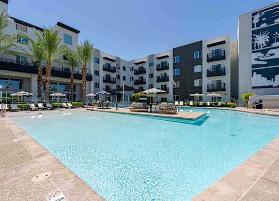 a large swimming pool with umbrellas and chairs in front of an apartment building