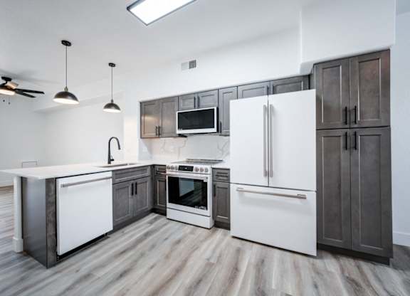 A modern kitchen with a white refrigerator, wooden floors, and dark brown cabinets.