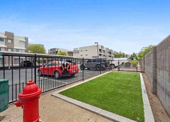 A red fire hydrant is in the foreground of a grassy area with a parking lot and buildings in the background.