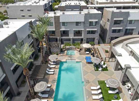 A swimming pool surrounded by palm trees and lounge chairs in a residential area.