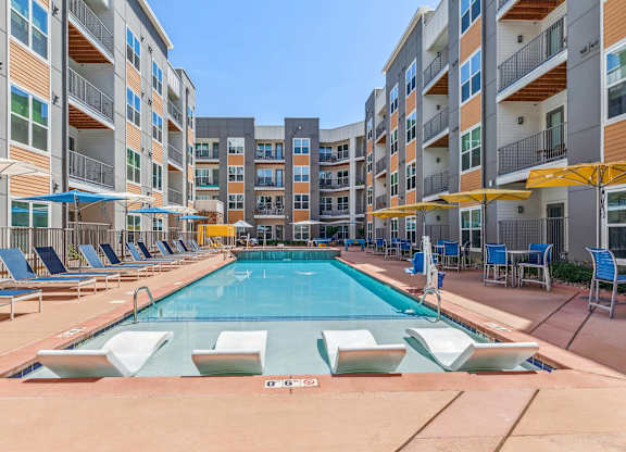 a swimming pool with chaise lounge chairs and umbrellas in front of an apartment building