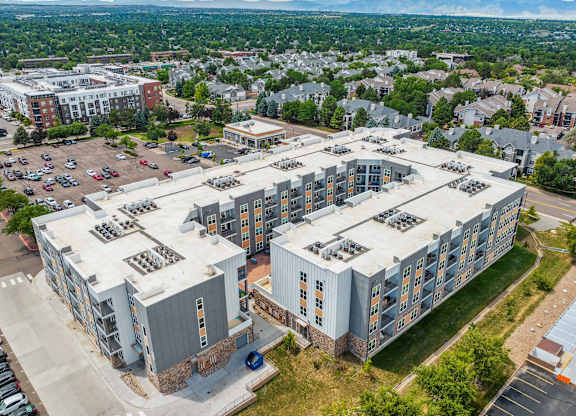 an aerial view of a large apartment building with a parking lot and a city in the background