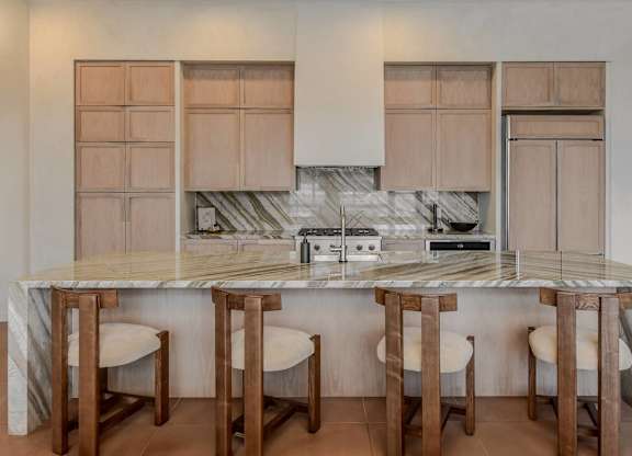 A kitchen with a marble countertop and wooden bar stools.