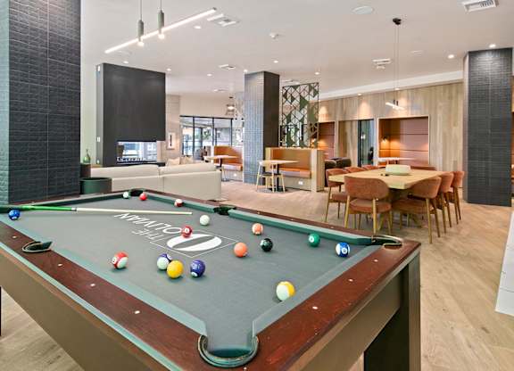 A pool table is in the middle of a room with a dining table and chairs.