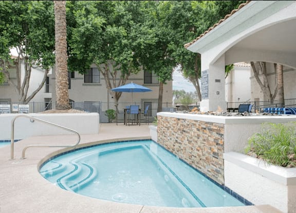 A small pool with a stone wall and a white building in the background.