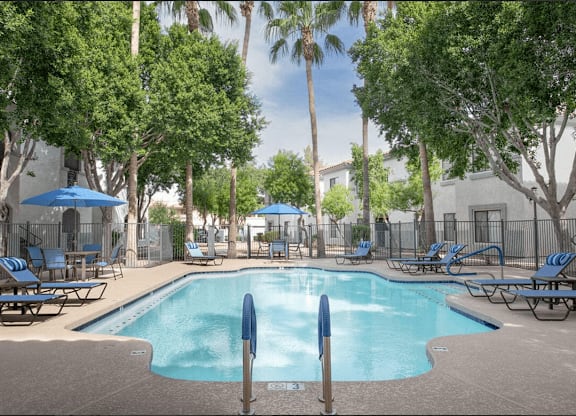 A pool surrounded by trees and chairs.