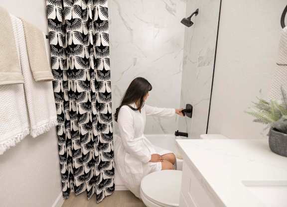 A woman in a white robe is sitting on a toilet in a bathroom.