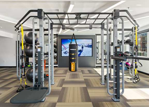 A gym with a variety of equipment including a squat rack, a bench, and a television.