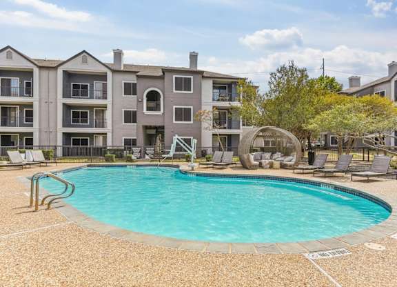 A large swimming pool is surrounded by a concrete patio and lounge chairs.