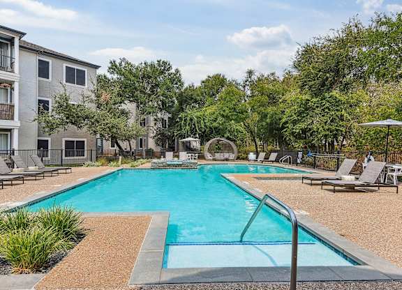 A swimming pool surrounded by trees and chairs.
