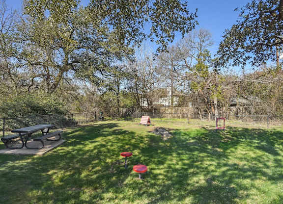 A park with a picnic table and a red object on the grass.
