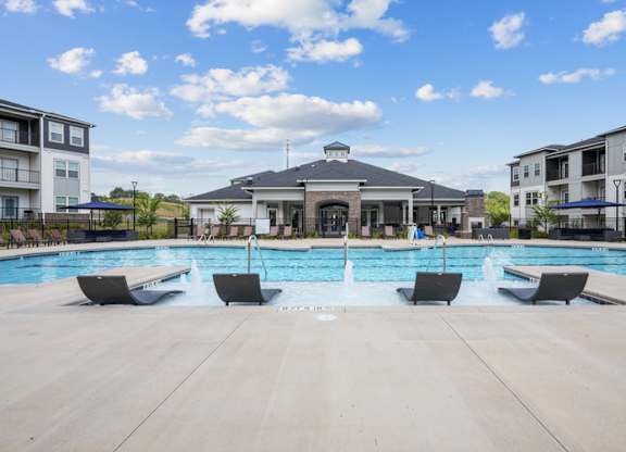 A large swimming pool with lounge chairs and a building in the background.
