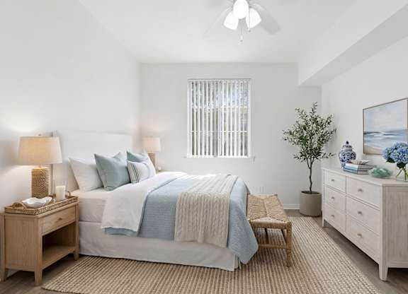 A bedroom with a bed, nightstand, and a plant.