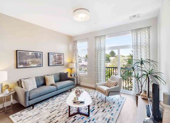A living room with a grey couch, a white coffee table, and a large window with curtains.