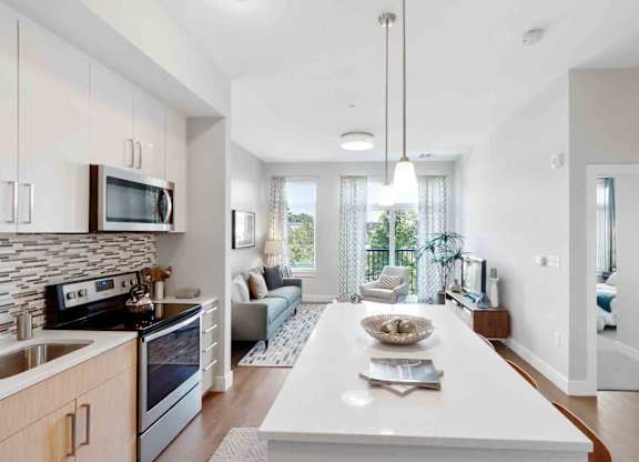 A modern kitchen with a white island and a dining area with a view.