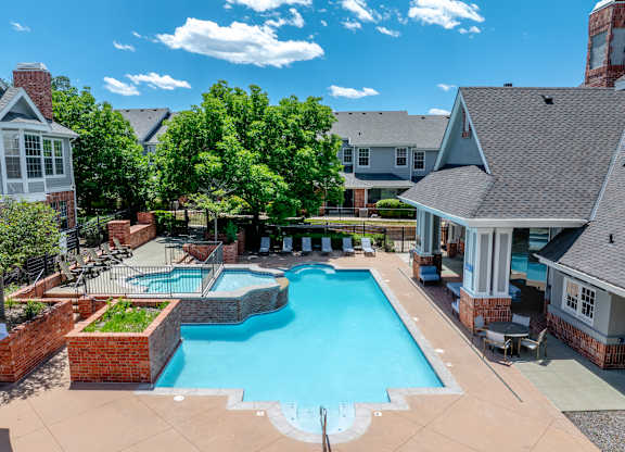 A large swimming pool surrounded by a brick wall and a patio area with chairs and a grill.