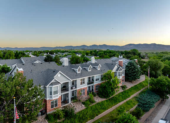 A large house with a flag on the left side is surrounded by greenery and has a mountain range in the background.