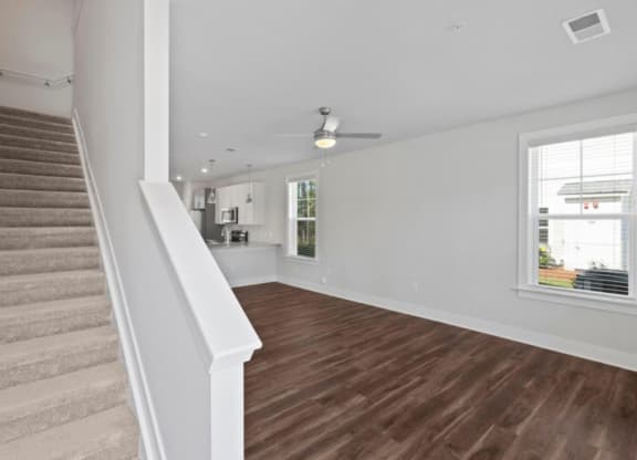 a living room with a staircase in the background and a kitchen in the foreground