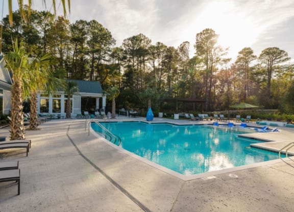 a swimming pool with chaise lounge chairs and trees in the background