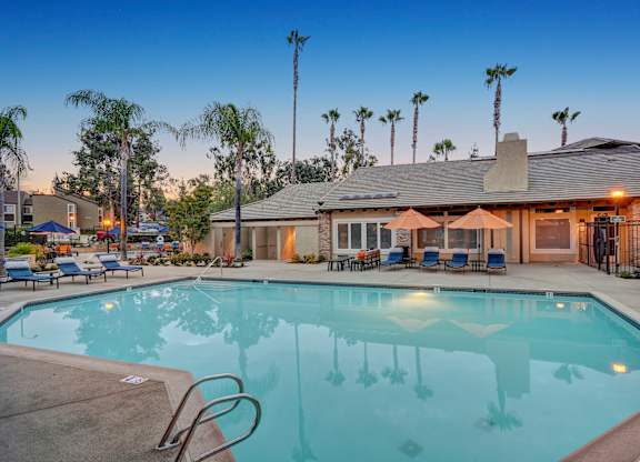 A swimming pool in front of a house with a patio and palm trees.