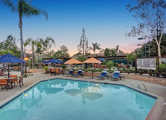 A large swimming pool surrounded by blue umbrellas and wooden benches.
