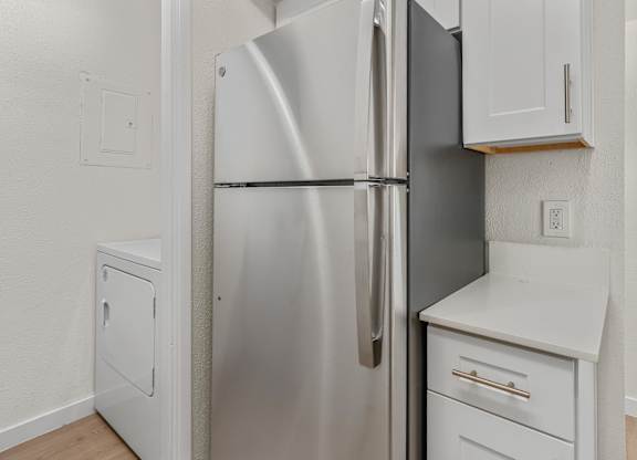 A stainless steel refrigerator stands in a kitchen with white cabinets and a white countertop.