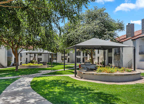 A gazebo is in the middle of a grassy area with a concrete walkway leading to it.