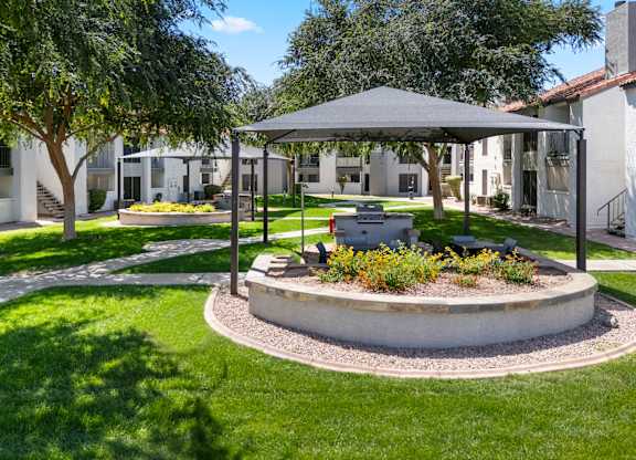A sunny day at a park with a pavilion and a fire pit.
