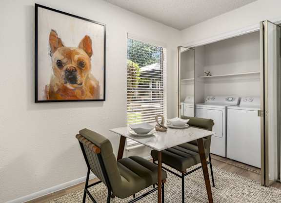 A kitchen with a table and chairs and a painting of a dog on the wall.