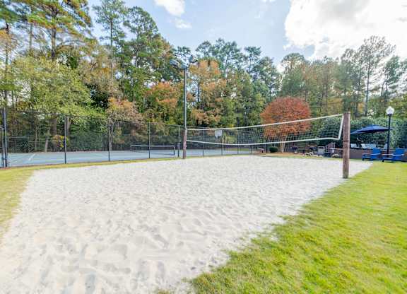 A sandy volleyball court surrounded by a fence and trees.