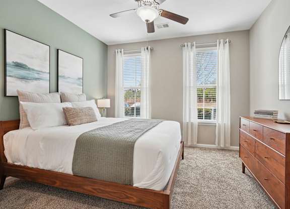 A bedroom with a bed, dresser, and window with curtains.