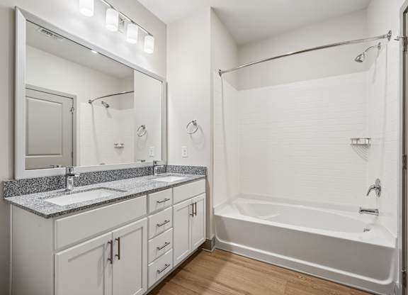 A white bathroom with a double sink vanity and a white bathtub.