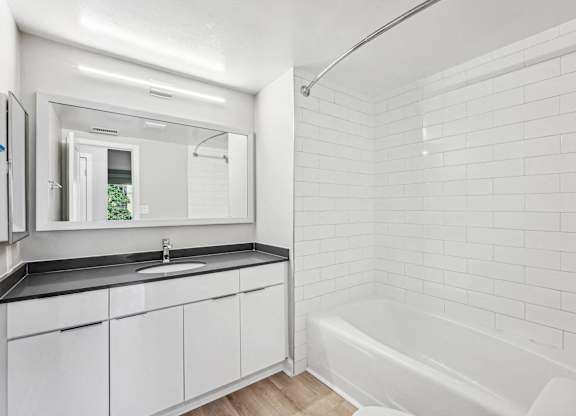 a white bathroom with a tub and a sink and a mirror