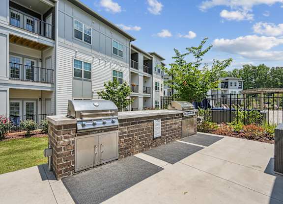 A brick wall with a grill on top is in front of apartment buildings.