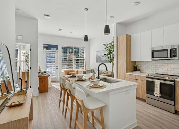 A modern kitchen with a long white island and wooden chairs.
