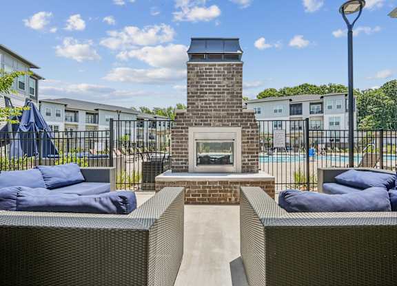 A patio with a fireplace and cushions is surrounded by a fence.