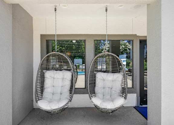 Two white hanging chairs with cushions are suspended from the ceiling in a room.