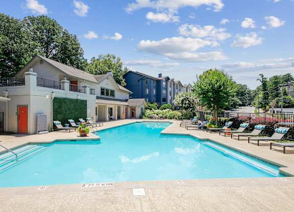 A large swimming pool surrounded by lounge chairs and trees.