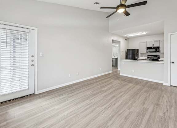 A room with a ceiling fan and light, a door with blinds, and a kitchenette in the background at Clear Creek Meadows Apartments, Copperas Cove, 76522