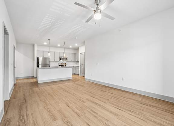 A room with a ceiling fan and a kitchen area in the background.