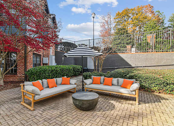 Two orange cushions on a grey sofa in a courtyard.