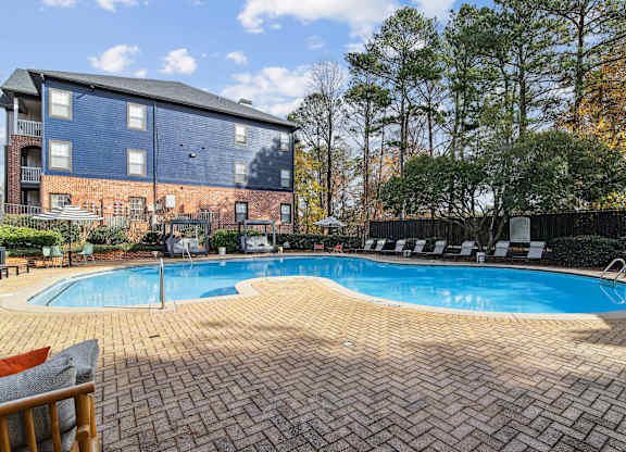 A swimming pool surrounded by a brick patio and a brick building in the background.