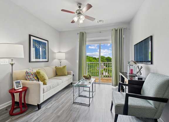 A living room with a white couch, a red side table, and a ceiling fan.